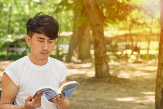 肖像年轻的男人。阅读书的公园夏天一天