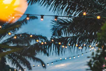 模糊光散景与椰子棕榈树背景日落黄色的字符串灯与散景装饰<strong>户外餐厅</strong>