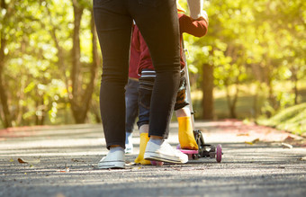 可爱的小孩子女孩有有趣的骑踏板车路与她的妈妈。夏天公园概念快乐家庭和童年关闭拍摄腿人花园