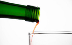 关闭倒水果汁从绿色瓶成玻璃孤立的白色背景