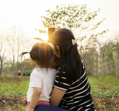 回来视图亚洲小孩子女孩采取照片与妈妈。花园在日落背景