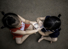亚洲小孩子坐着的花园和饲料一些牛奶她的妹妹从玻璃食物健康概念