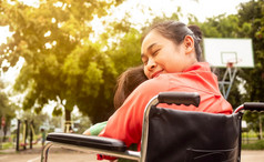 快乐妈妈。轮椅拥抱小女孩坐着她的腿上的公园禁用母亲概念
