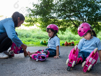 年轻的妈妈。帮助她的女儿把保护垫和安全头盔之前她的辊滑冰实践的公园路活跃的户外体育运动为孩子们