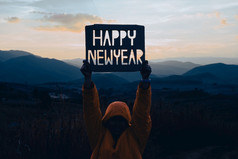 手持有快乐新一年设计从纸板对的背景山与日落快乐新一年概念