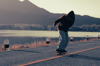 滑板者滑板湖边路日落年轻的快乐男孩溜冰者练习滑板日落