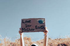 手持有持有海报与单词爱你的妈妈。地球对的背景蓝色的天空气候改变概念