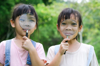 孩子们学习和探索自然与户外放大玻璃好奇的孩子看起来通过放大玻璃的树的公园两个小姐妹玩与放大玻璃