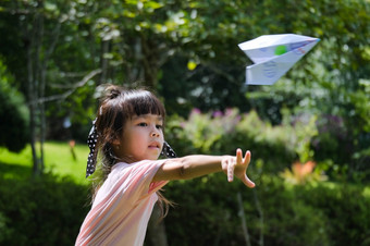 快乐孩子们玩与纸飞机的夏天花园可爱的小女孩扔纸飞机的公园快乐童年概念
