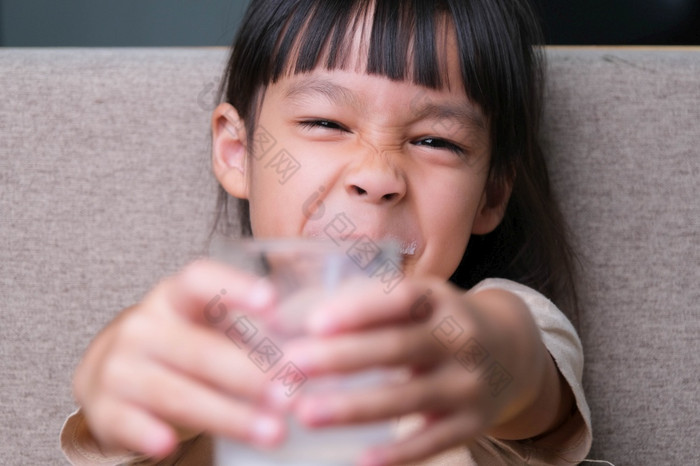 肖像可爱的亚洲小女孩持有玻璃牛奶坐着的沙发首页小女孩首页与微笑脸感觉快乐享受喝牛奶和看相机
