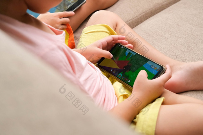 两个小女孩上瘾移动手机亚洲姐妹是玩游戏看漫画与他们的智能手机的沙发首页