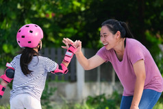 亚洲妈妈。帮助女儿实践辊滑冰的公园令人兴奋的户外活动为孩子们