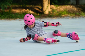 可爱的亚洲小女孩保护垫和安全头盔练习辊滑冰的公园令人兴奋的户外活动为孩子们学龄前儿童穿辊溜冰鞋瀑布下来