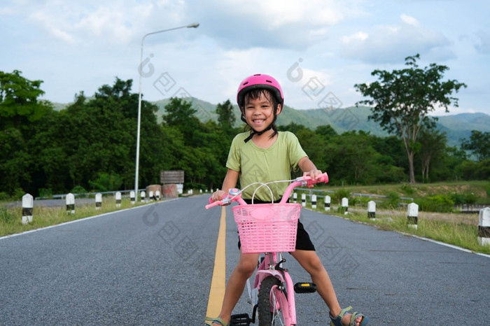 可爱的小女孩头盔骑自行车沥青路夏天快乐小女孩骑自行车在户外健康的夏天活动为孩子们