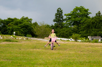 可爱的亚洲小女孩骑自行车的草坪上热夏天一天快乐小女孩骑自行车在户外健康的夏天活动为孩子们