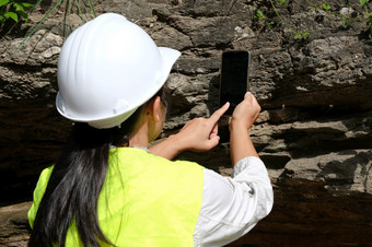 亚洲女地质学家研究员分析岩石与智能手机自然公园探索地质学家的场石头和生态概念