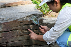 亚洲女地质学家研究员分析岩石与放大玻璃自然公园探索地质学家的场石头和生态概念