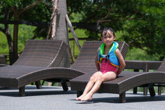 小女孩泳衣坐在休息室椅子的池阳光明媚的一天和微笑的相机夏天生活方式概念