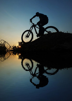 男人。骑自行车轮廓日落反射河