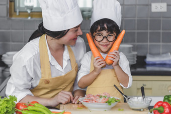 亚洲女人年轻的<strong>妈妈</strong>。与儿子男孩烹饪沙拉食物与蔬菜持有两个胡萝卜和西红柿贝尔<strong>辣</strong>椒为快乐家庭烹饪食物享受生活方式厨房