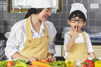 亚洲女人年轻的妈妈。与儿子男孩烹饪沙拉食物与蔬菜持有两个西红柿和胡萝卜贝尔辣椒为快乐家庭烹饪食物享受生活方式厨房