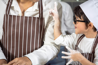 亚洲男孩穿眼镜<strong>取</strong>笑爸爸烹饪与白色面粉揉捏面包面团教孩子们实践烘焙成分面包蛋<strong>餐具</strong>厨房生活方式快乐学习生活与家庭