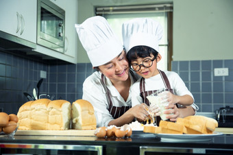亚洲男孩穿眼镜取笑<strong>爸爸</strong>烹饪与白色面粉揉捏面包面团教孩子们实践烘焙成分面包蛋餐具<strong>厨房</strong>生活方式快乐学习生活与家庭