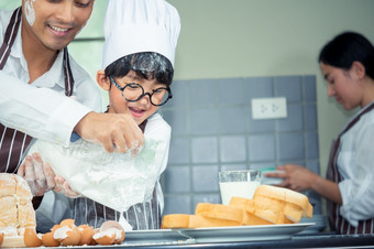 亚洲男孩穿眼镜<strong>取</strong>笑爸爸烹饪与白色面粉揉捏面包面团教孩子们实践烘焙成分面包蛋<strong>餐具</strong>厨房生活方式快乐学习生活与家庭