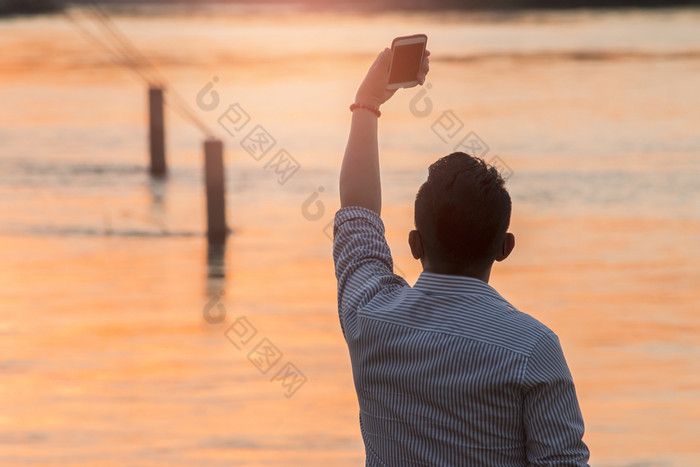 年轻的男人。采取自拍图片使用他的智能海绵享受日落时间在户外