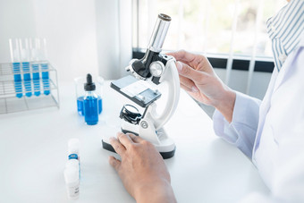 科学家女人医疗脸面具<strong>使用显微镜</strong>和测试管与蓝色的液体而工作研究和实验关于冠状病毒疫苗实验室