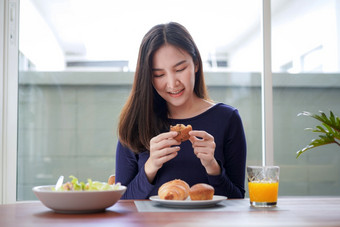 年轻的亚洲女人持有和有位吃面包与玻璃新鲜的橙色汁后吃健康的沙拉早餐健康生活方式首页