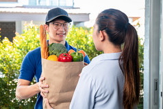 亚洲交付男人。蓝色的统一的持有杂货店袋食物水果蔬菜给女人客户前面房子那服务在冠状病毒新冠病毒流感大流行