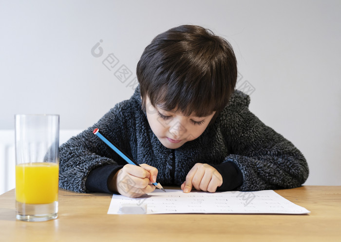 肖像可爱的孩子坐着独自一人做家庭作业与快乐脸可爱的孩子男孩使用铅笔写作白色纸学生做拼写测试homehomeschooling概念