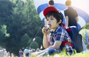 坦诚的拍摄孩子坐着草场吃巧克力与模糊的人背景饿了孩子男孩吃甜蜜的而等待为热空气气球准备好了<strong>发布</strong>夏天户外<strong>活动</strong>