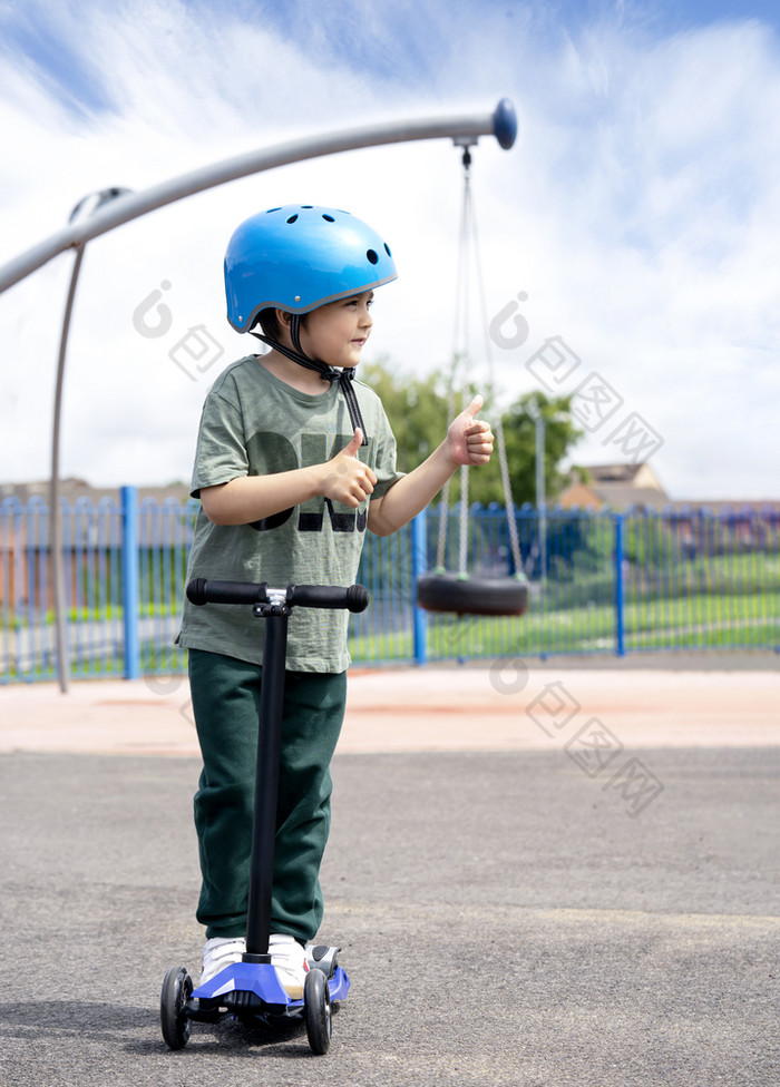 肖像男孩显示拇指而站踏板车操场上阳光明媚的一天夏天孩子安全头盔骑辊孩子玩在户外活跃的休闲和户外体育运动为孩子们
