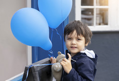 可爱的小男孩与泰迪熊持有蓝色的气球与微笑脸快乐孩子玩与空气气球户外孩子有有趣的玩外春天夏天