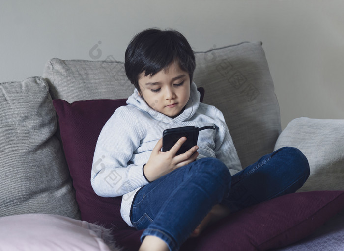 孩子男孩坐着沙发看漫画移动电话学校孩子使用手机学习教训互联网而学校从首页学校教育距离学习在线教育概念