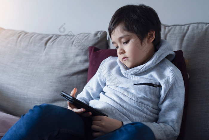 孩子自我隔离使用手机为家庭作业伤心孩子坐着沙发看下来深认为男孩学习互联网从首页在学校首页学校教育学习在线教育