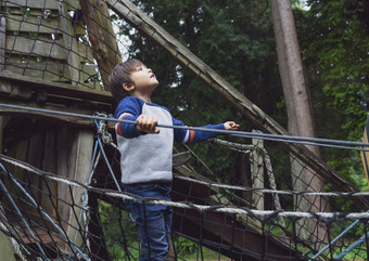 肖像活跃的孩子攀爬绳子框架树屋年轻的男孩站独自一人和看高森林树附近的公园孩子玩户外操场上独自一人秋天