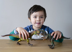 活跃的小男孩玩与恐龙玩具木表格首页快乐孩子有有趣的玩与他的两个恐龙战斗为他的放松时间孩子们发展和想象力概念