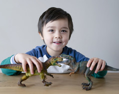 活跃的小男孩玩与恐龙玩具木表格首页快乐孩子有有趣的玩与他的两个恐龙战斗为他的放松时间孩子们发展和想象力概念