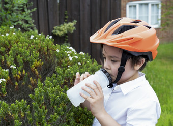 健康的孩子穿自行车头盔喝水渴了男孩持有瓶水健康的孩子与新鲜的脸后喝水而骑自行车世界水一天孩子们健康哪