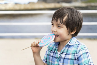 有趣的孩子吃棒棒糖快乐小男孩持有大糖糖果孩子与微笑脸吃糖果活跃的童年享受欢乐时光户外阳光明媚的一天夏天