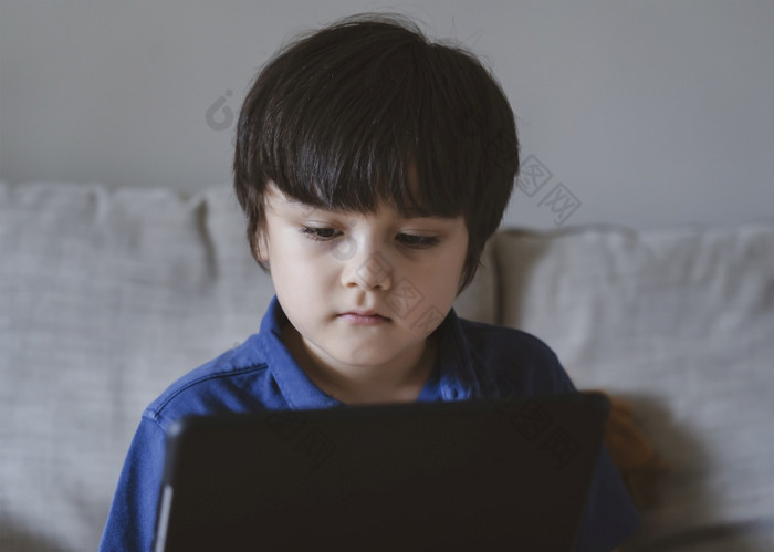 学校孩子使用平板电脑为他的家庭作业孩子看数字平板电脑与思考脸年轻的男孩看卡通触摸垫正常的生活睑腺炎与学习在线距离教育