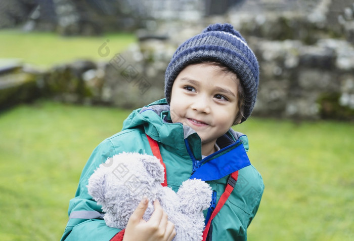 肖像学校孩子采取泰迪熊探索与他的学习历史快乐孩子男孩穿温暖的布持有他的软玩具坐着老砖墙与模糊的废墟老修道院背景