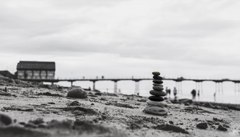 卵石塔的海边与模糊的码头下来的海堆栈Zen岩石石头的沙子石头金字塔的海滩象征着稳定和谐平衡与浅深度场