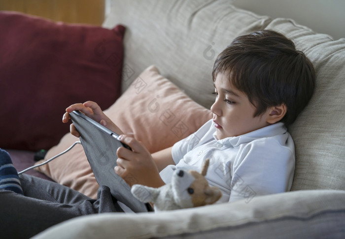 孩子男孩坐着沙发看漫画移动电话学校孩子使用手机学习教训互联网首页学校教育距离学习在线教育概念