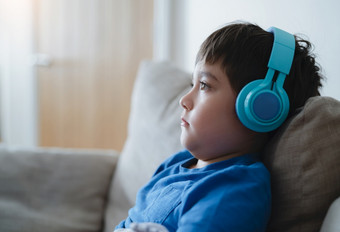 一边视图肖像孩子男孩穿耳机和看出深认为学校男孩蓝色的t恤听音乐可爱的孩子坐着沙发放松生活房间首页