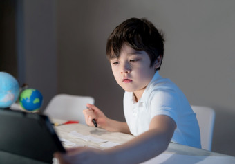 学校孩子使用平板电脑为他的家庭<strong>作业</strong>孩子男孩做家庭<strong>作业</strong>使用数字平板电脑搜索信息互联网后回来从学校电子学习首页学校教育教育概念