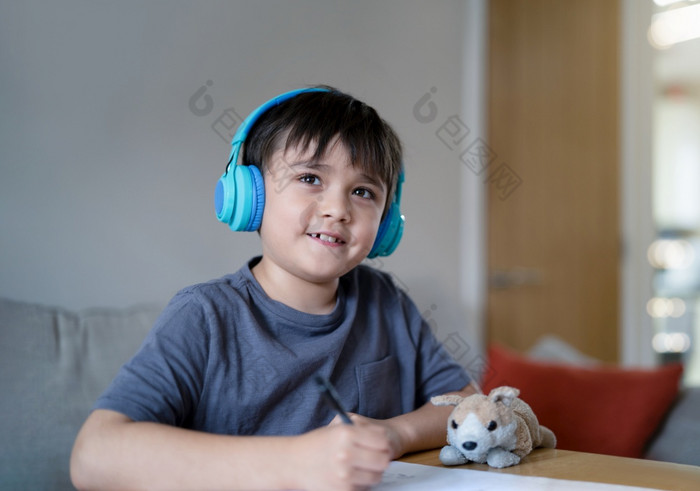 快乐孩子穿耳机听音乐而画纸在室内肖像可爱的年轻的男孩看与微笑脸积极的孩子享受有创意的活动首页周末